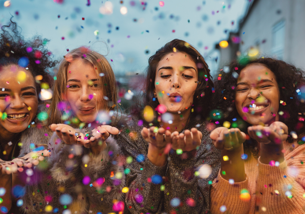 Young women blowing confetti from hands. Women blowing confetti